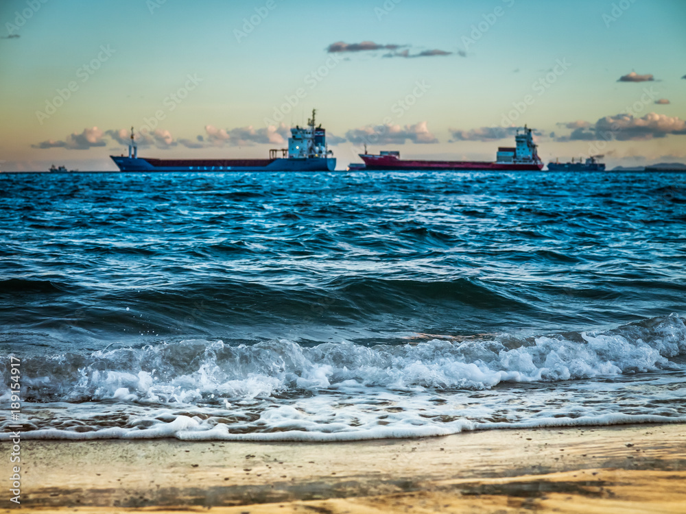 splashing waves on the beach and vessels in the background