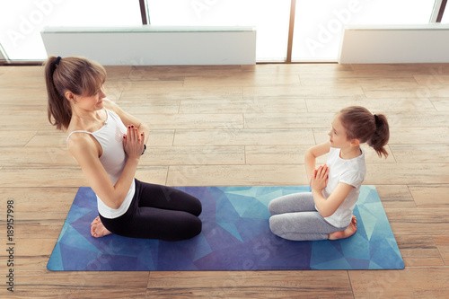 Young mother and little kid daughter in the gym centre doing yoga or stretching fitness exercise together. Healthy lifestyle concept