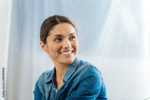 Sincere smile. Appealing kind young woman posing on the light background while grinning and looking aside