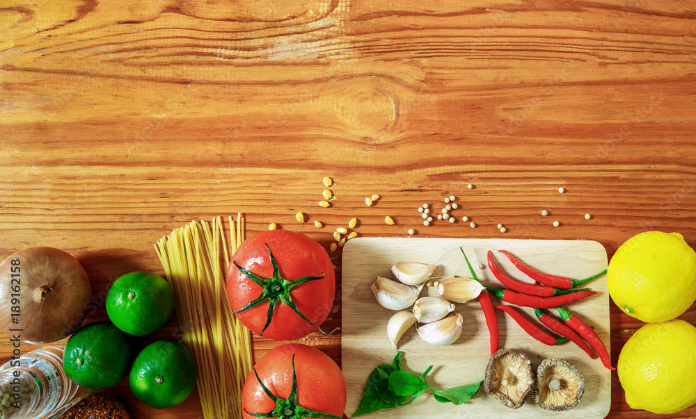 pasta ingredients on wooden table in kitchen, spaghetti,tomato,garlic,mushroom,line,lemon, chilli, pepper on cutting board