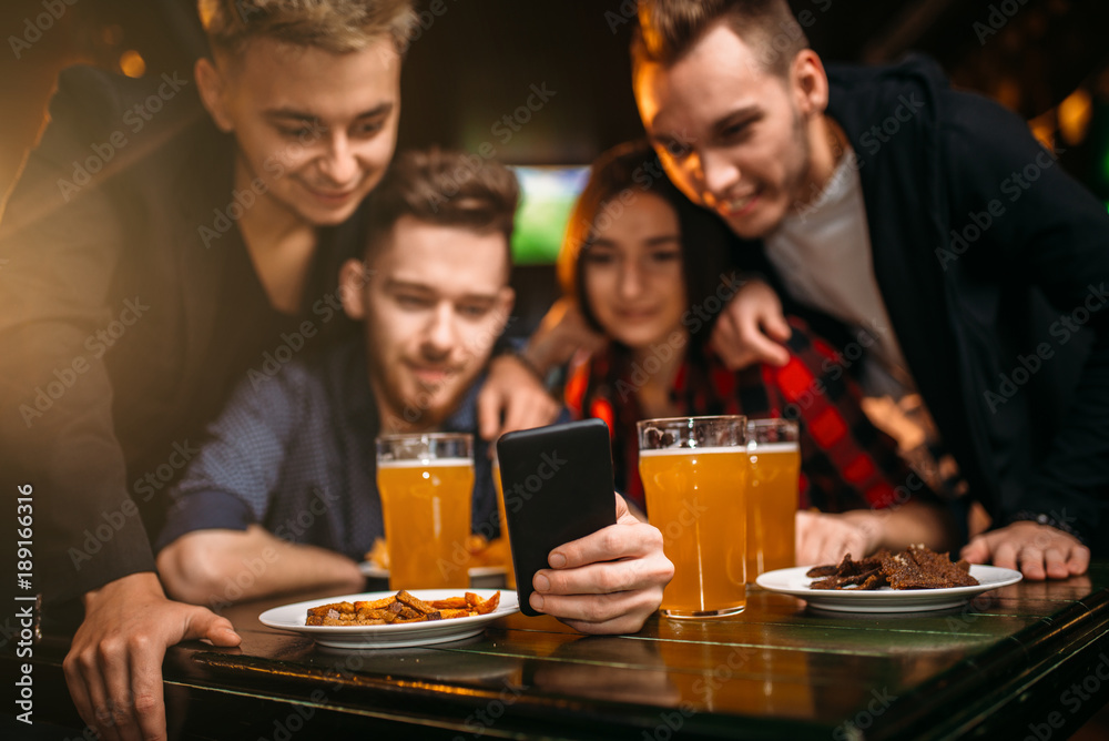 Fun company watches photo on phone in a sport bar Fun company watches photo on phone in a sport bar