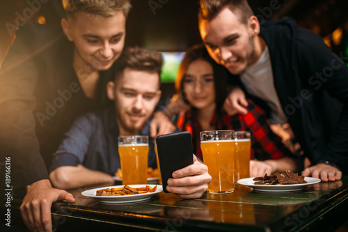 Fun company watches photo on phone in a sport bar