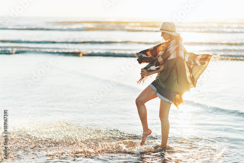 Charming young girl with poncho, hat, sunglasses with beautiful smile having fun on the beach at sunset in warm weather. © Alex from the Rock