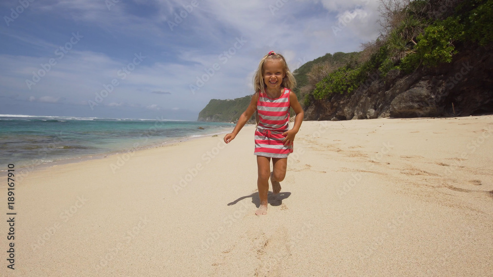 Little, pretty girl runs along a tropical beach of the sea and have fun. Cute happy girl has fun on vacation at sea. Bali,Indonesia. Travel concept.