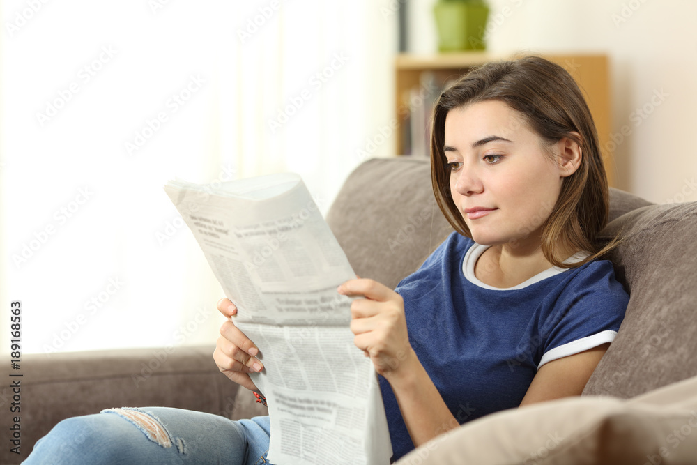 Serious teenager reading a newspaper at home Serious teenager reading a newspaper at home