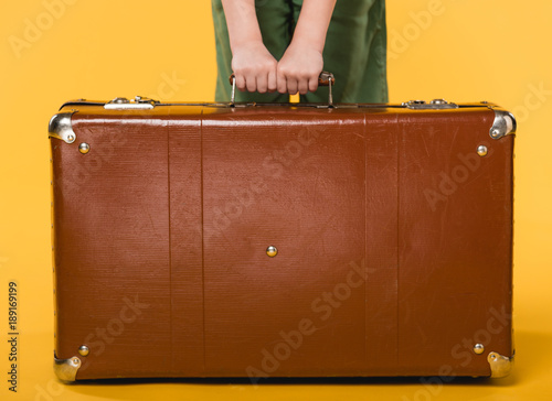 partial view of child holding leather suitcase isolated on yellow