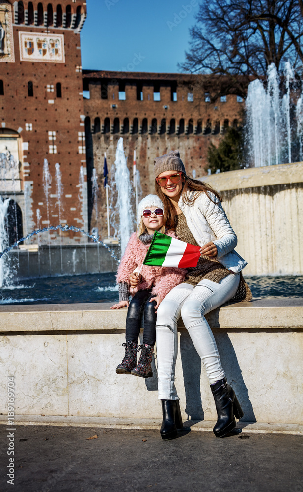 smiling mother and child tourists in Milan, Italy showing flag
