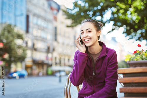 a young smiling woman tourist in sportswear seets on the bench in the center of Prague with a phone in the hands of. travel guide, tourism in Europe, woman tourist with smartphone on the street photo