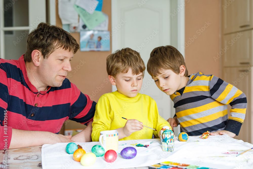 Two little kid boys and father coloring eggs for Easter holiday in domestic kitchen Two little kid boys and father coloring eggs for Easter holiday in domestic kitchen