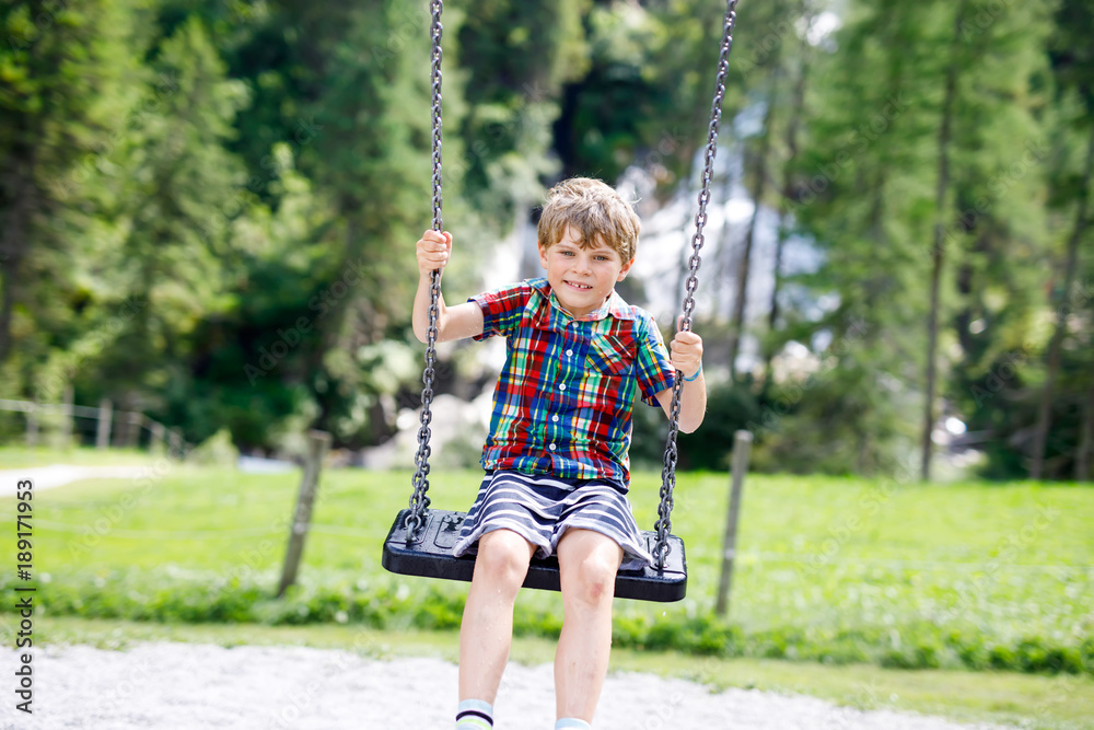 Funny kid boy having fun with chain swing on outdoor playground during rain Funny kid boy having fun with chain swing on outdoor playground during rain