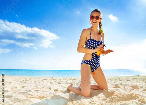 Carta da parati smiling young woman in swimsuit on seashore with SPF