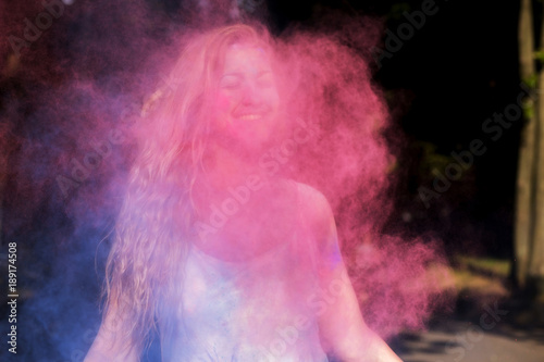Positive young model with curly hair having fun in a cloud of pink powder at Holi festival of colors