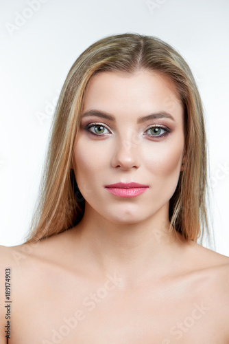 Fullface type enface portrait of a blonde green-eyed model with makeup on, including eyeshadows, lipstick and face contouring. Photo made on a white background in a professional photo studio.