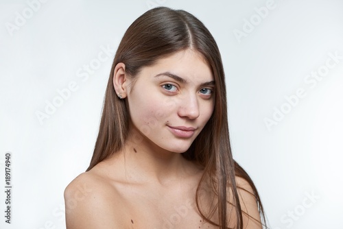Fullface type half profile portrait of a young beautiful brunette model with green eyes being naural and without makeup on her face. Photo made on a white background in a professional photo studio.