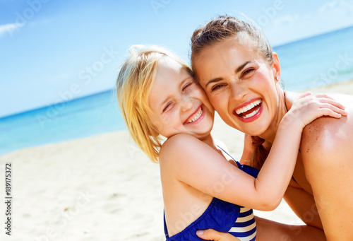 smiling healthy mother and daughter on seashore embracing
