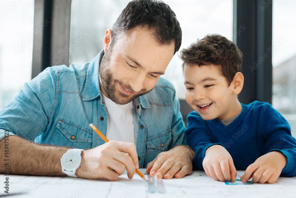 Under supervision. Upbeat little boy sitting at the table next to his  father and watching him draw a blueprint with a pencil and a ruler Stock  Photo | Adobe Stock
