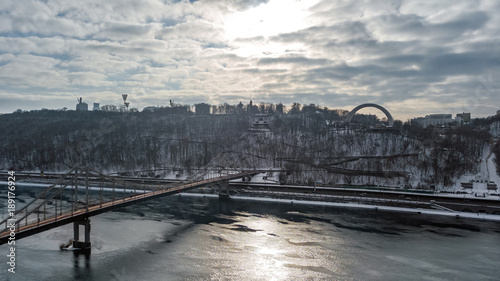 Aerial top view of pedestrian Park bridge in winter and Dnieper river from above, snow Kyiv cityscape, city of Kiev skyline, Ukraine 