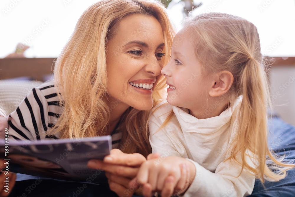 I cherish you. Loving joyful blond mother and her little daughter smiling and reading a magazine and mom caressing her I cherish you. Loving joyful blond mother and her little daughter smiling and reading a magazine and mom caressing her