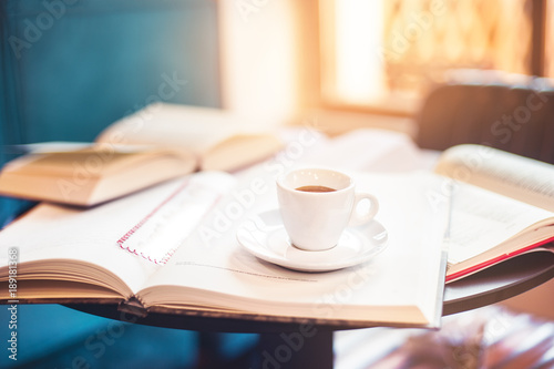 front view Cup of espresso among a lot of opened books sun light in background