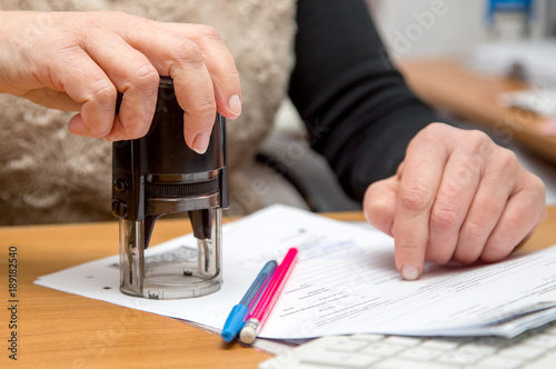 Tablou pe pânză Female hand with a stamp puts a seal on a blank