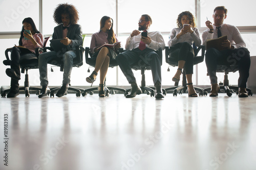 Large group of business people sitting on office chairs on big window background.