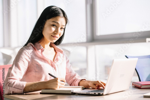 Close up image of beautiful female employee in office. Making notes at desk.