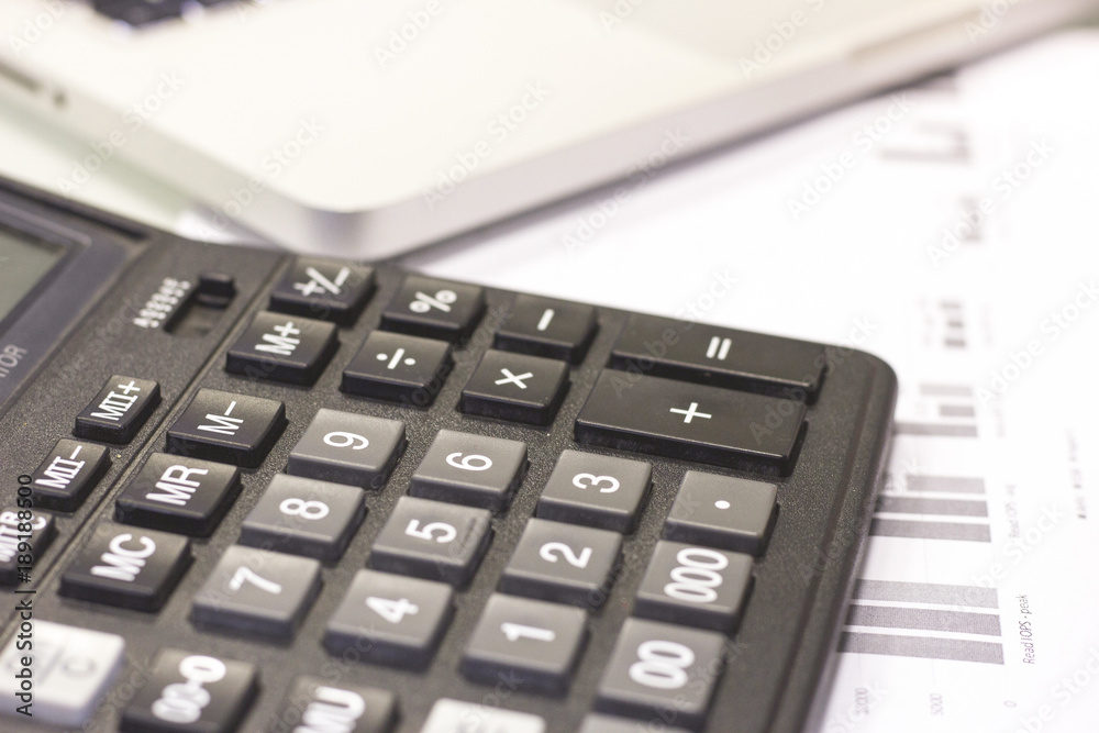 Business, Finance, Analysis concept. A workplace with a calculator, papers with stock charts and graphs and a laptop, close up Business, Finance, Analysis concept. A workplace with a calculator, papers with stock charts and graphs and a laptop, close up