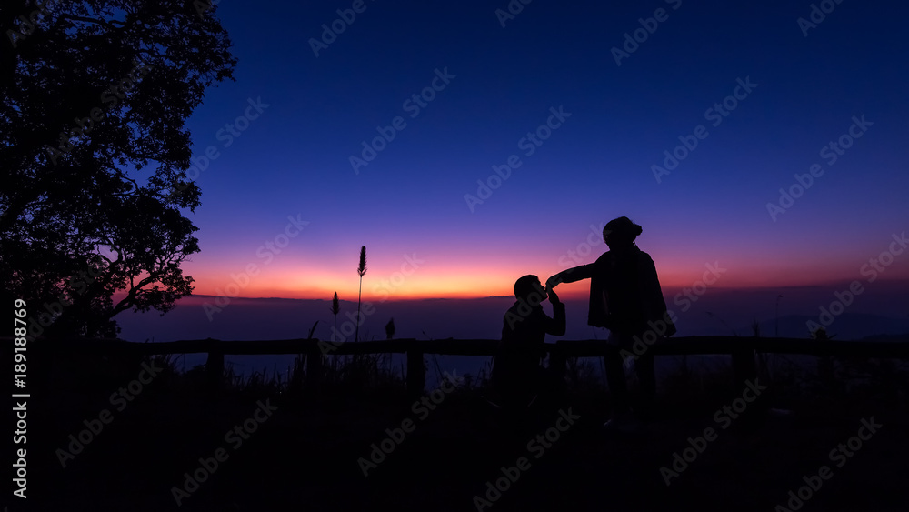 The silhouette of women and men is watching the sunset happily.