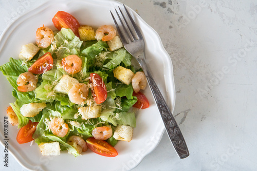 Caesar salad with shrimps in a white plate top view