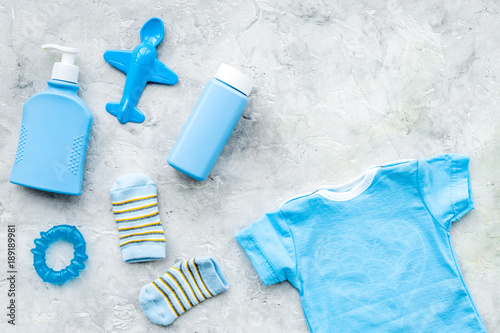 Blue set for newborn boy. Baby bodysuit, socks, airplan toy, soap and powder on grey background top view