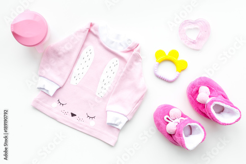 Cute pink baby clothes for girl. Shirt, booties, toy, bottle on white background top view copy space