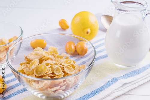 Bowl with corn flakes, jug of milk and empty bowl for prepared delicious breakfast.The concept of healthy breakfast, corn flakes with milk and fruit on wooden table, close up.