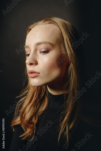 Closeup portrait of female with closed eyes in black pullover over dark studio background.