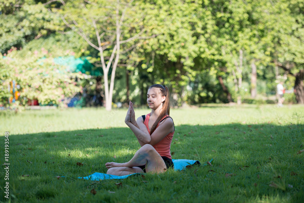 Young woman practicing yoga in the park outdoor. Concept of healthy lifestyle and relaxation.