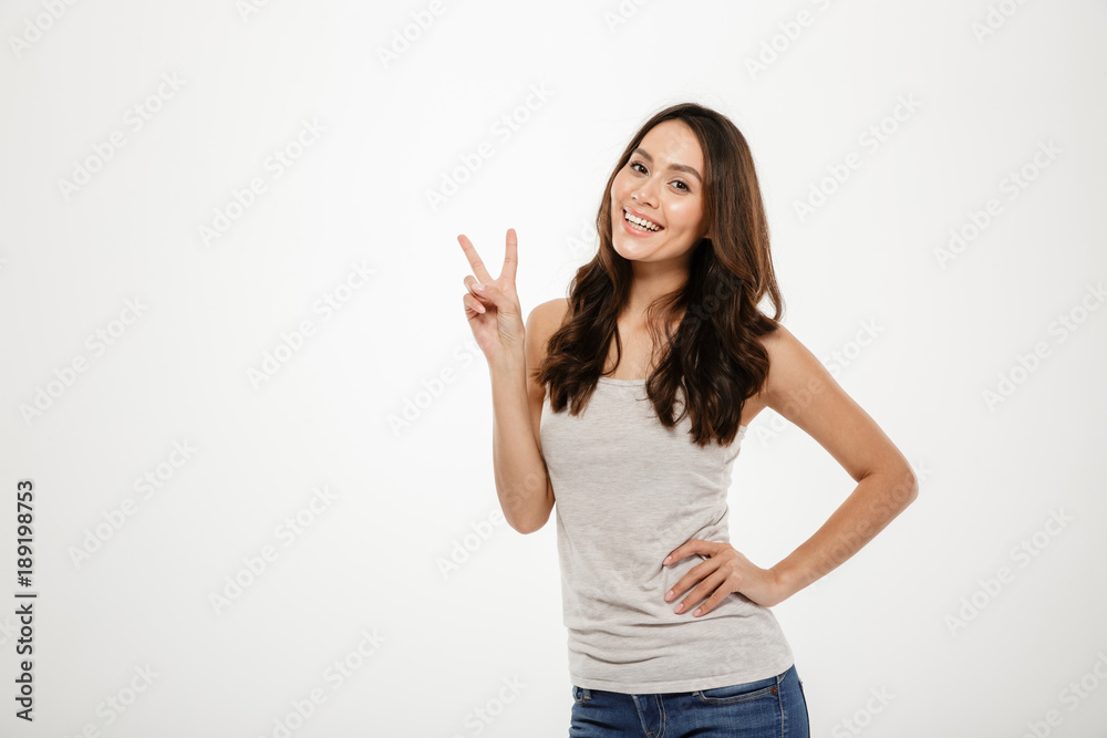 Smiling brunette woman with arm on hip showing peace gesture Smiling brunette woman with arm on hip showing peace gesture