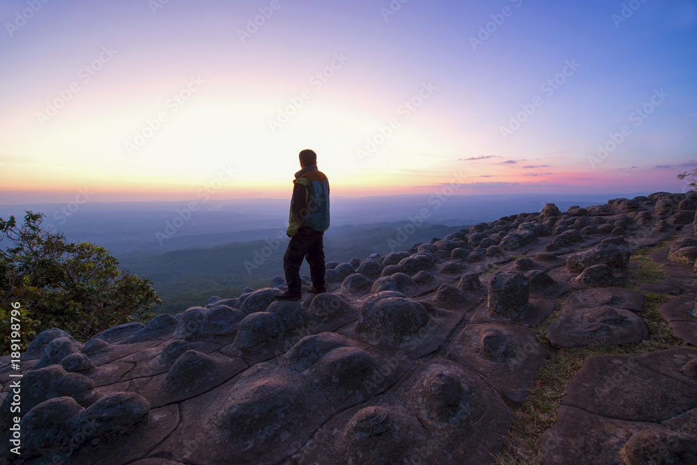 Hiking man is stading on the rock of the moutian while sunset.
