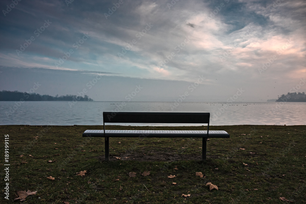 An empty bench by the lake at sunset.