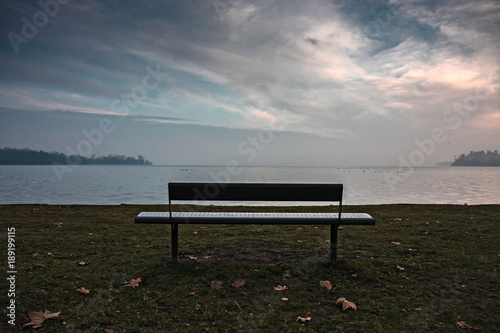 An empty bench by the lake at sunset.