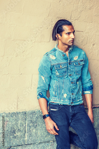 Obraz na płótnie Portrait of Young East Indian American Man in New York. Young handsome man wearing blue fashionable Denim jacket, standing by painted wall, looking away, thinking.. w salonie