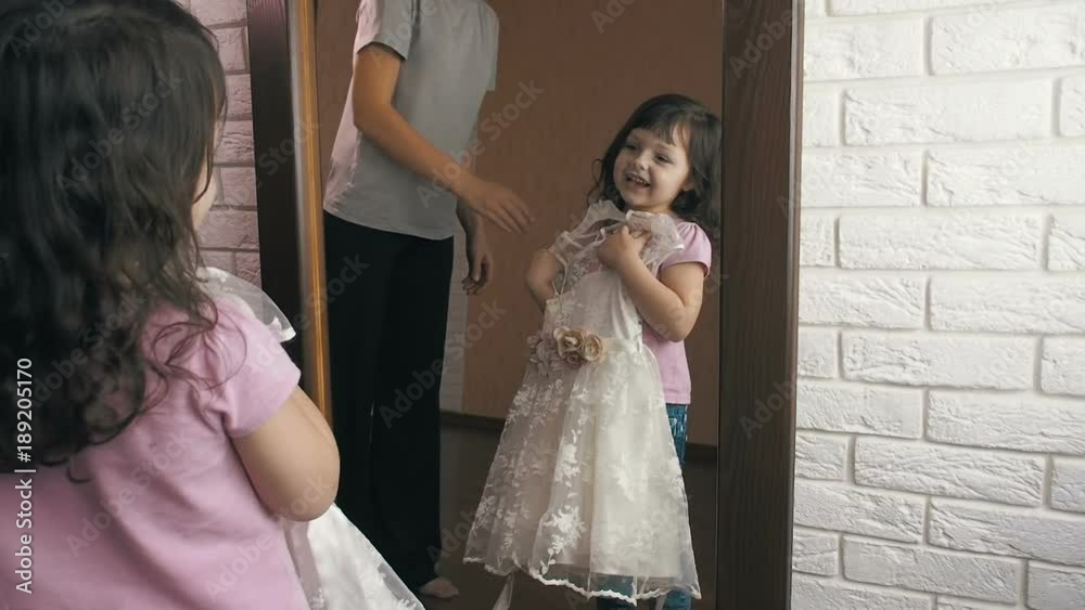 The child at the mirror. Mom gives a beautiful little daughter a little dress. The child at the mirror. Mom gives a beautiful little daughter a little dress.