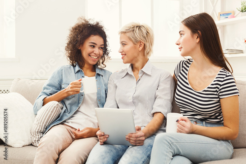 Three happy female friends using tablet and drinking coffee