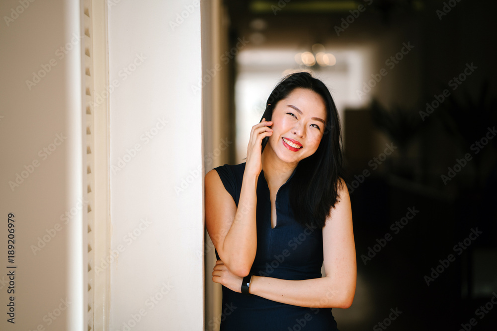 Portrait of a professional businesswoman standing in the middle of a corridor and talking on the phone. She appears to be smiling. Portrait of a professional businesswoman standing in the middle of a corridor and talking on the phone. She appears to be smiling.