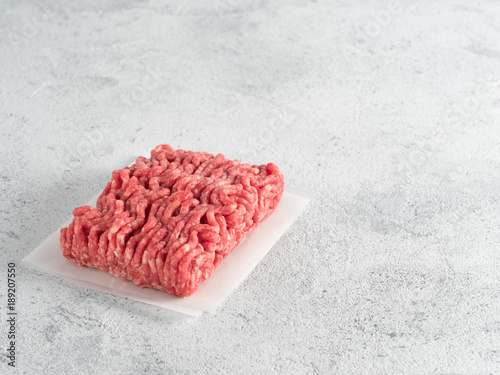 Φωτογραφία Fresh raw minced beef on backing paper over light gray cement background with copy space
