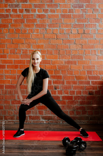 Portrait of beautiful blonde woman in black sportswear standing against the background of a red brick wall after fitness workout.Fites concept. The girl does warm-up before a fitness training.