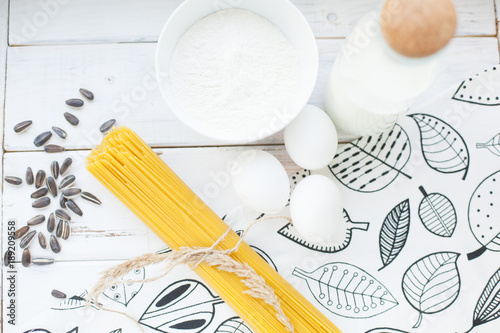 Cooking Homemade Spaghetti with eggs  flour  milk and sunflower seeds on a white wooden table and white tablecloth with floral pattern  selective focus  top view