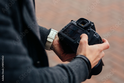 Photographer holding professional camera looks at photos, outdoors. Close-up.