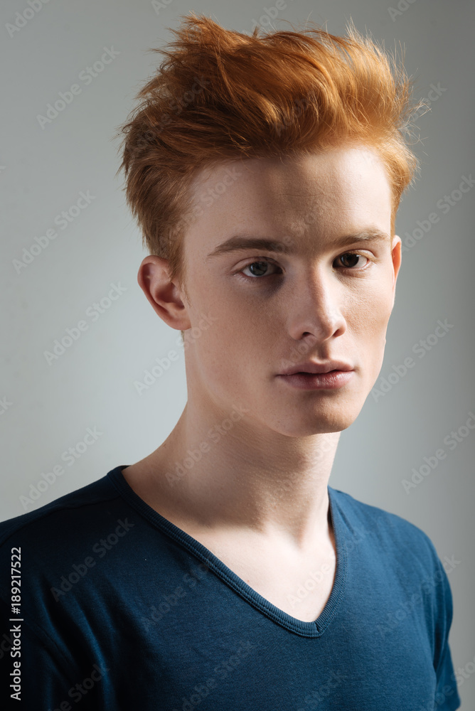 Haircut. Good-looking stern dark-eyed red-haired young man wearing a t-shirt and staring and having a stylish haircut Haircut. Good-looking stern dark-eyed red-haired young man wearing a t-shirt and staring and having a stylish haircut