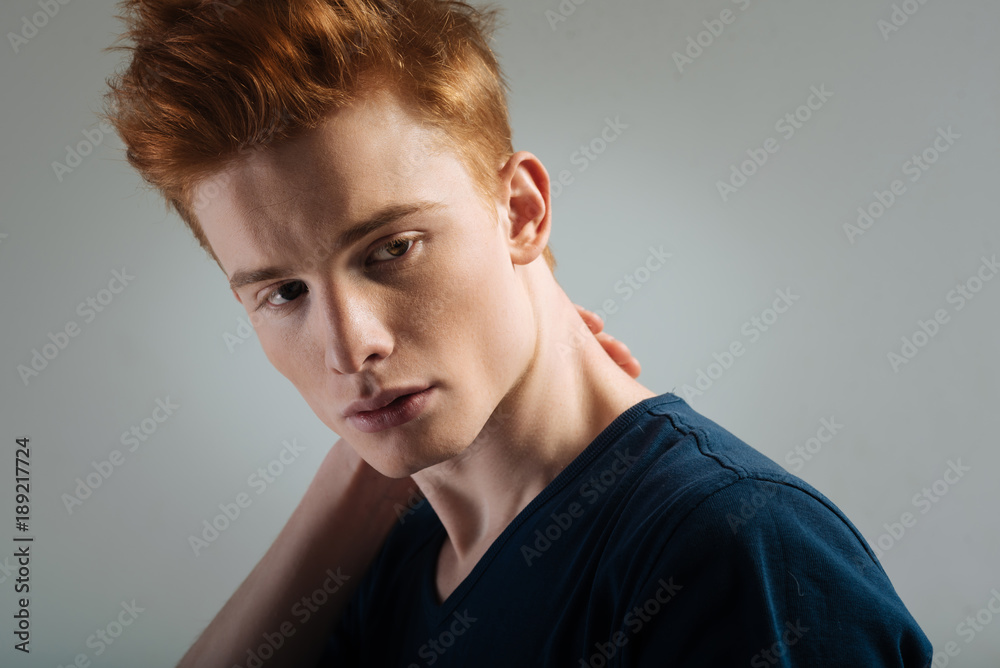 Thoughts. Good-looking upset red-haired young man looking sadly and thinking and touching his neck Thoughts. Good-looking upset red-haired young man looking sadly and thinking and touching his neck