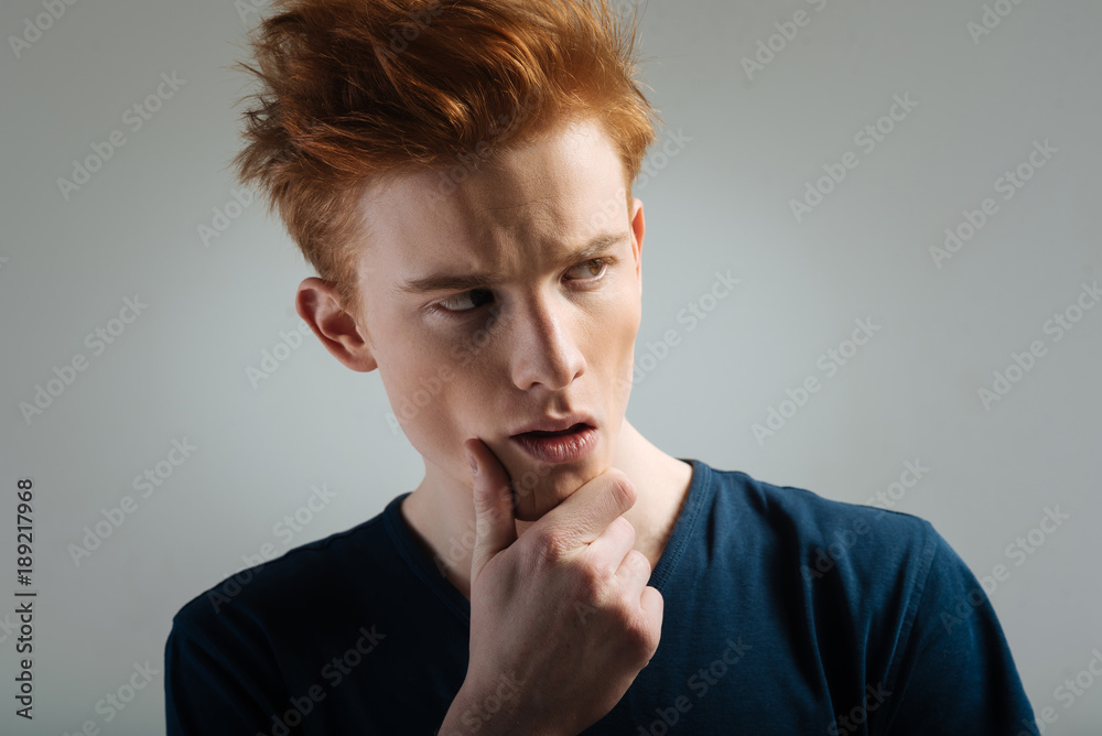 Making a decision. Handsome thoughtful red-haired young man thinking and looking in the distance and touching his chin Making a decision. Handsome thoughtful red-haired young man thinking and looking in the distance and touching his chin