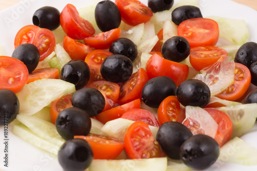 Greek salad with vegetables, feta cheese, black olives in process. Wooden background . Top view